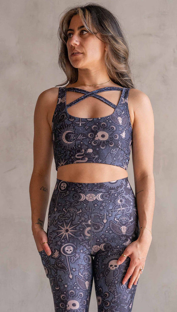 Front view of model wearing WERKSHOP Four-Way Reversible Top. The top has a tarot card themed artwork on a dark blue background on one side and a zodiac themed artwork on purple background on the opposite side. She is wearing it with the Blue side out and the X neckline detail in the front.