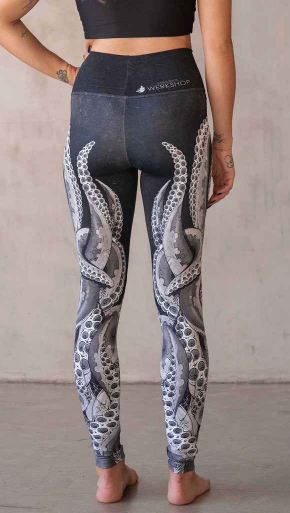 Back view of model wearing WERKSHOP Tentacles Athleisure Leggings. The artwork on the leggings features hand drawn tentacles wrapping up and around each leg in colors of black and white with distressed texture.