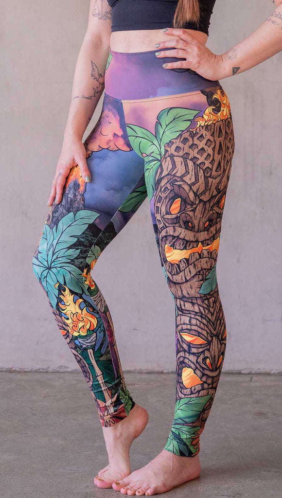 Model wearing WERKSHOP Tiki Tiki Time leggings featuring original and exclusive artwork of a Tiki Totem with fire, palm trees and a cotton candy colored sunset. 