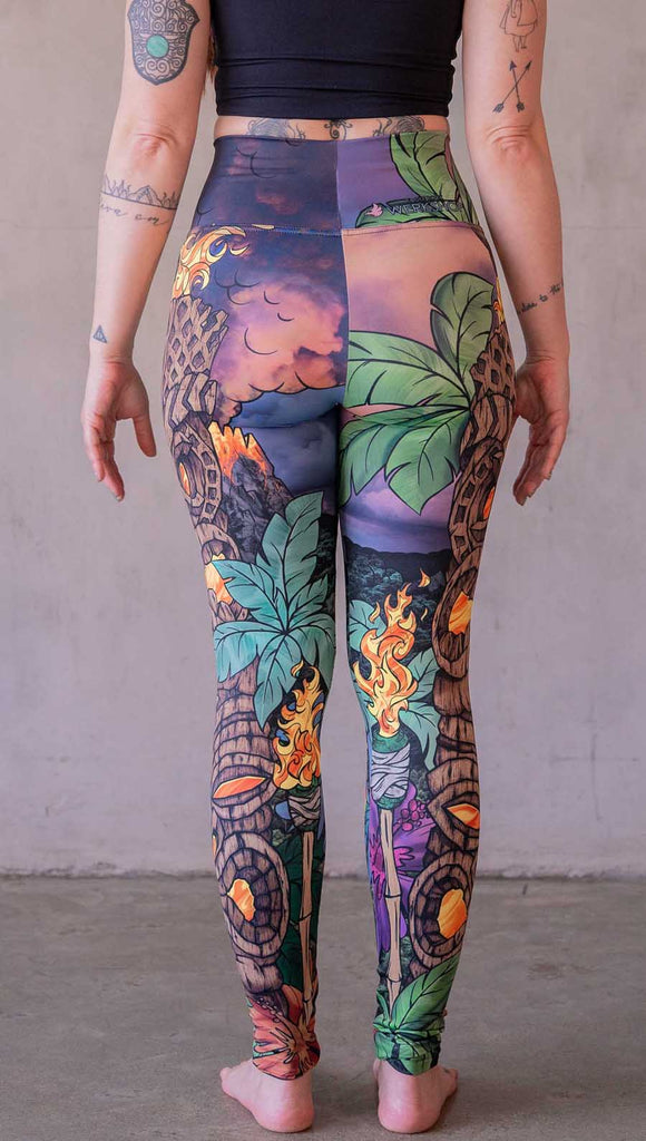 Model wearing WERKSHOP Tiki Tiki Time leggings featuring original and exclusive artwork of a Tiki Totem with fire, palm trees and a cotton candy colored sunset. 