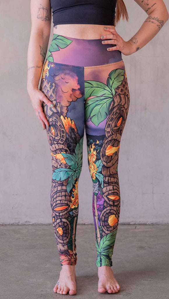 Model wearing WERKSHOP Tiki Tiki Time leggings featuring original and exclusive artwork of a Tiki Totem with fire, palm trees and a cotton candy colored sunset. 