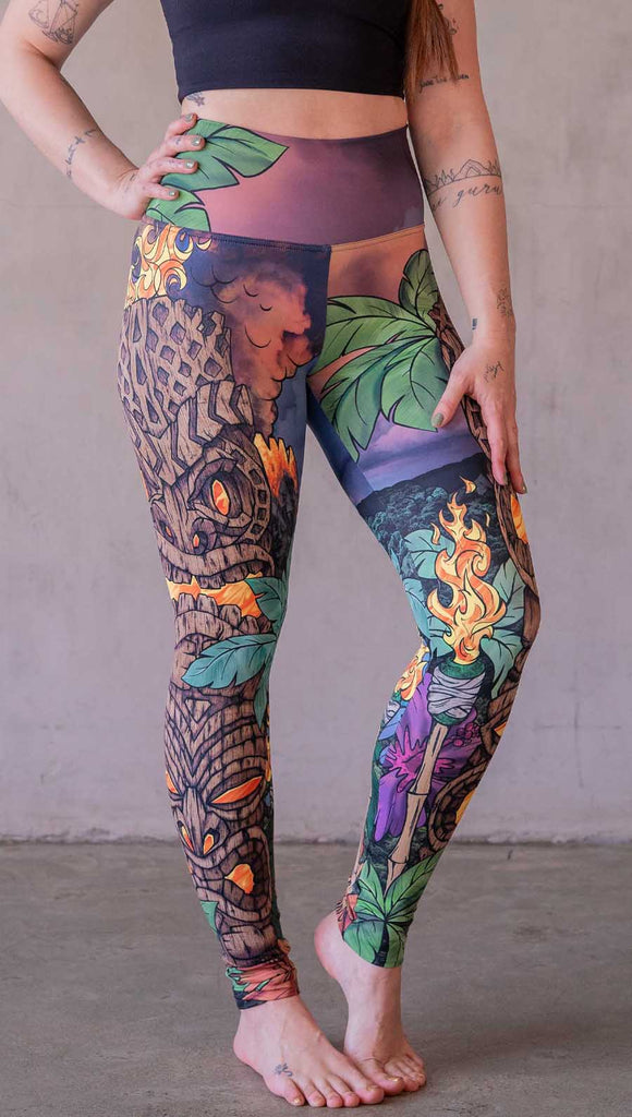 Model wearing WERKSHOP Tiki Tiki Time leggings featuring original and exclusive artwork of a Tiki Totem with fire, palm trees and a cotton candy colored sunset. 