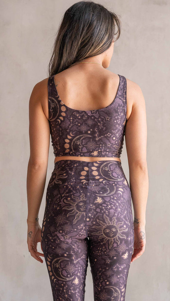 Front view of model wearing WERKSHOP Four-Way Reversible Top. The top has a tarot card themed artwork on a dark blue background on one side and a zodiac themed artwork on purple background on the opposite side. She is wearing it with the Purple side out and the X neckline detail in the front .