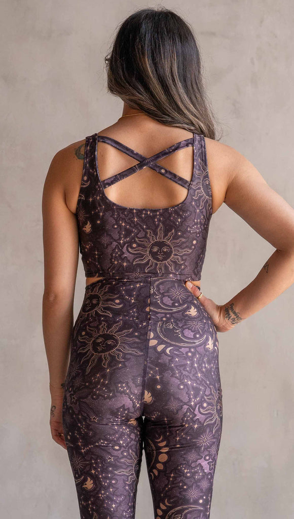 Front view of model wearing WERKSHOP Four-Way Reversible Top. The top has a tarot card themed artwork on a dark blue background on one side and a zodiac themed artwork on purple background on the opposite side. She is wearing it with the Purple side out and the X neckline detail in the front across her back.