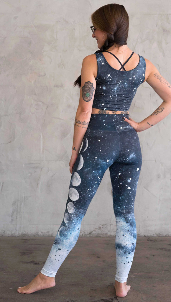 back view of a girl wearing our moon phases athleisure leggings - with the phases of the moon printed on the wearer's left leg on a starry night sky with all zodiac constellations in the background
