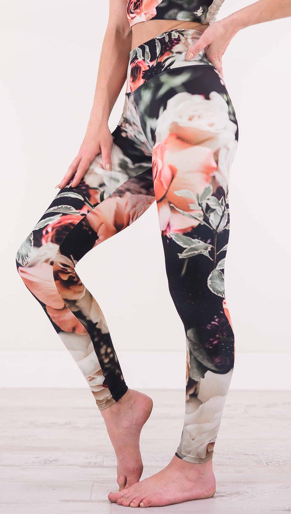 Enhanced left view of model wearing black athleisure leggings with pink and white roses and leafy greens throughout