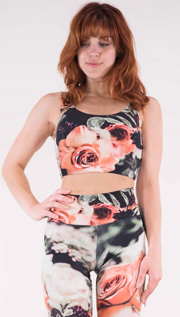 Front view of model wearing the Bodacious Bouquet reversible crop top. It is a black color with pink and white roses and leafy greens throughout