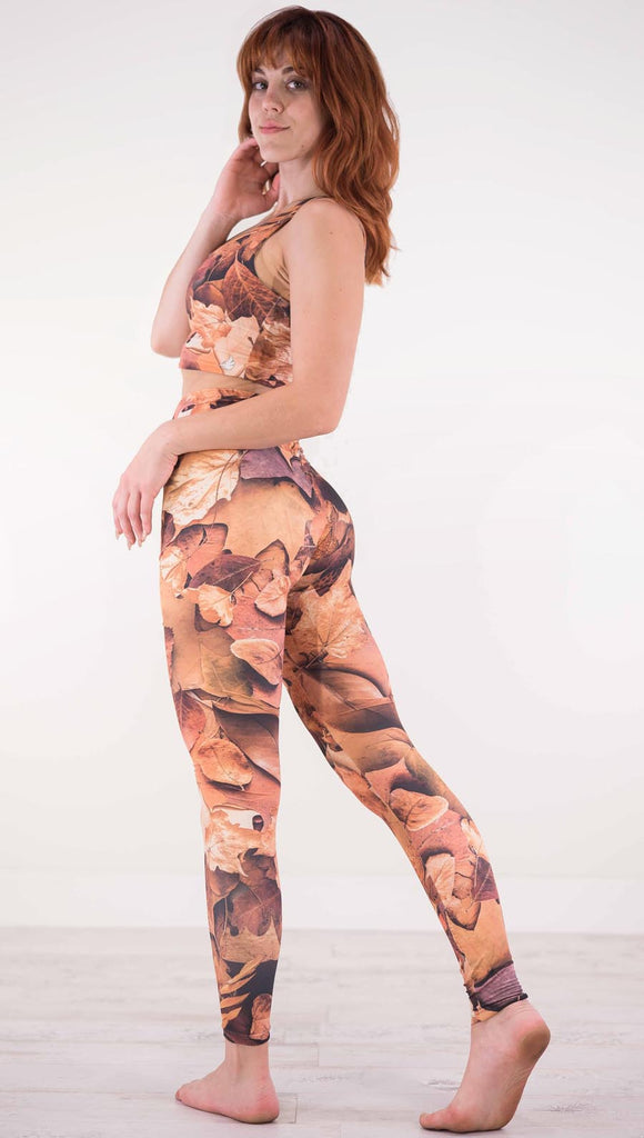 Back view of model wearing athlleisure leggings that have different shades of orange autumn leaves