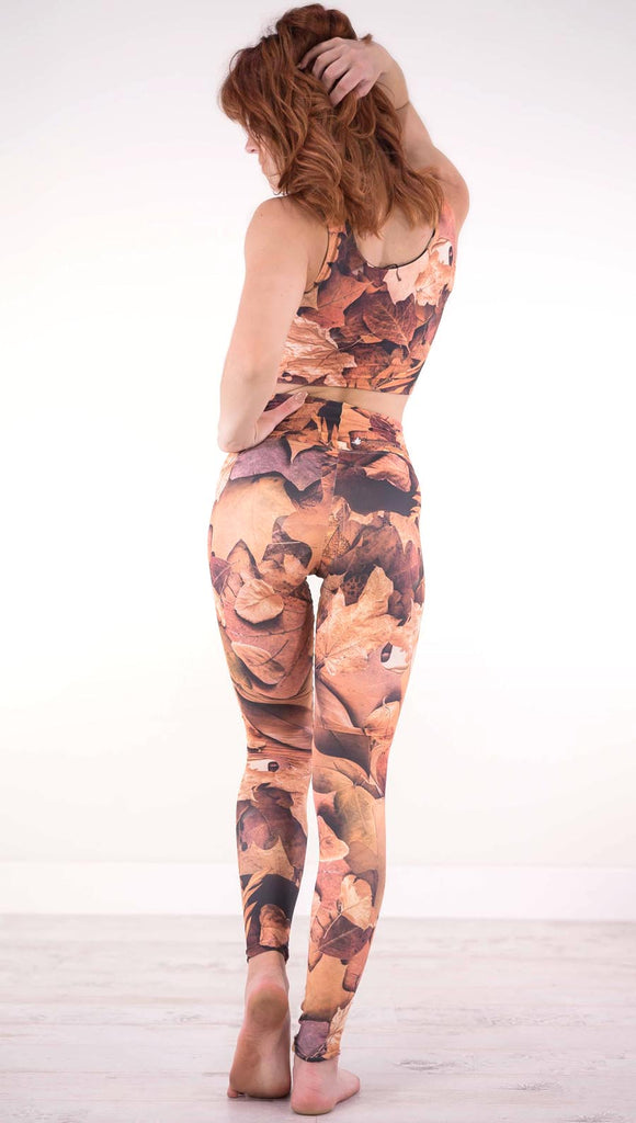 Back view of model wearing athleisure leggings that have different shades of orange autumn leaves