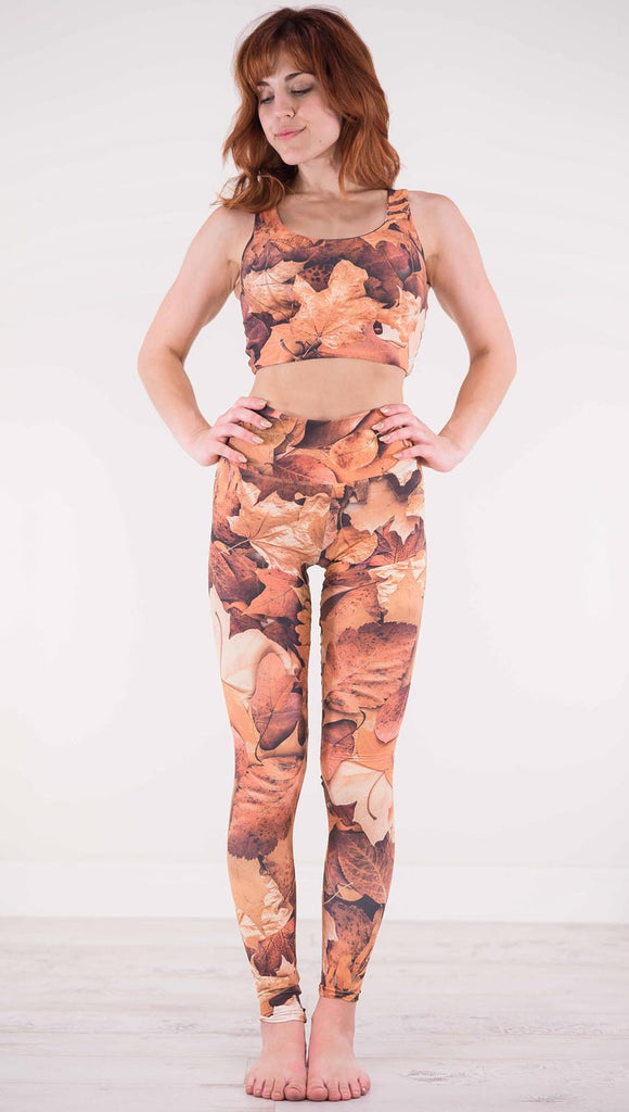 Front view of model wearing athleisure leggings that have different shades of orange autumn leaves 