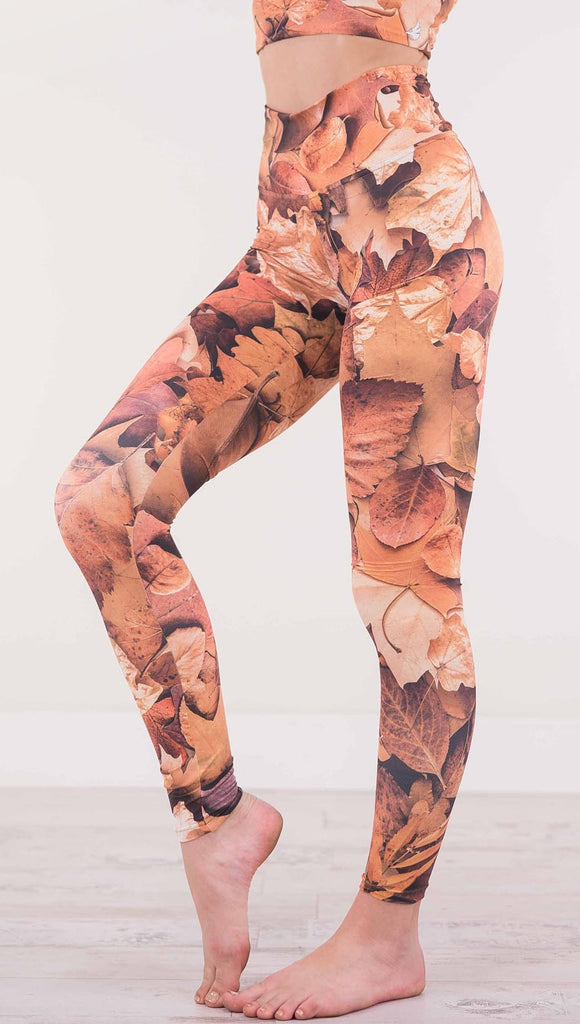 Enhanced left view of model wearing athleisure leggings that have different shades of orange autumn leaves
