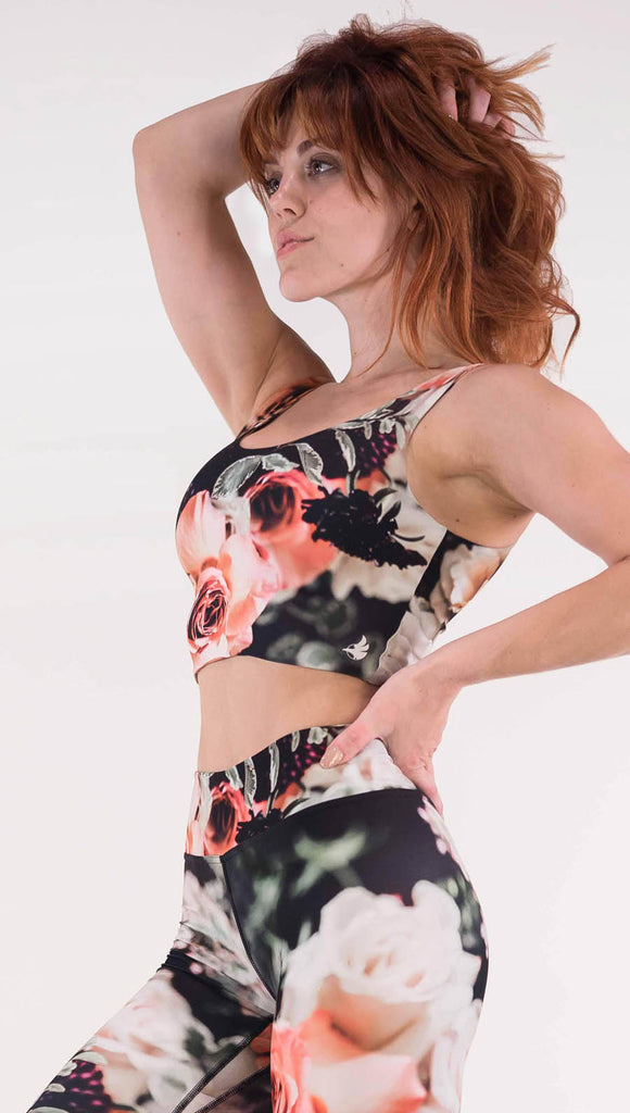 Left view of model wearing the Bodacious Bouquet reversible crop top. It is a black color with pink and white roses and leafy greens throughout