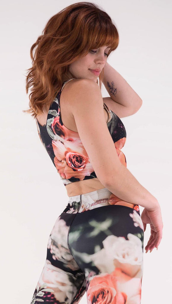 Back view of model wearing the Bodacious Bouquet reversible crop top. It is in a black color with pink and white roses and leafy greens throughout 