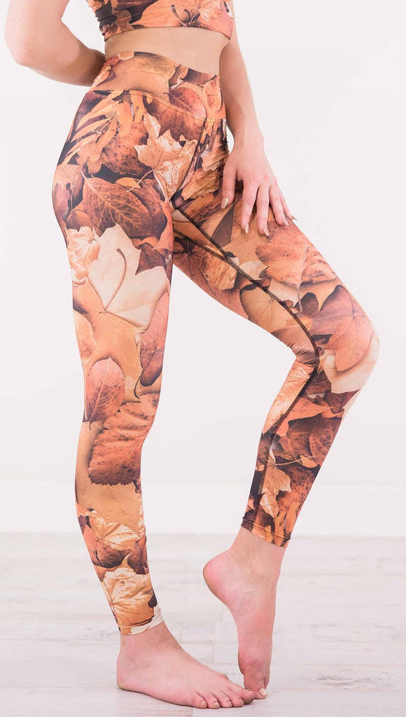 Right view of model wearing triathlon leggings that have different shades of orange autumn leaves