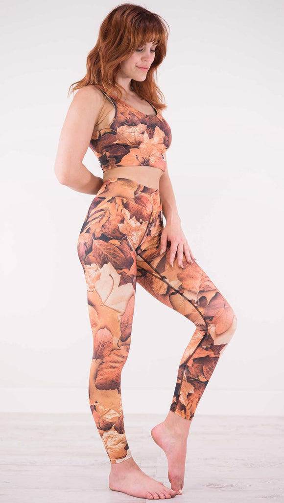 Right view of model wearing triathlon leggings that have different shades of orange autumn leaves