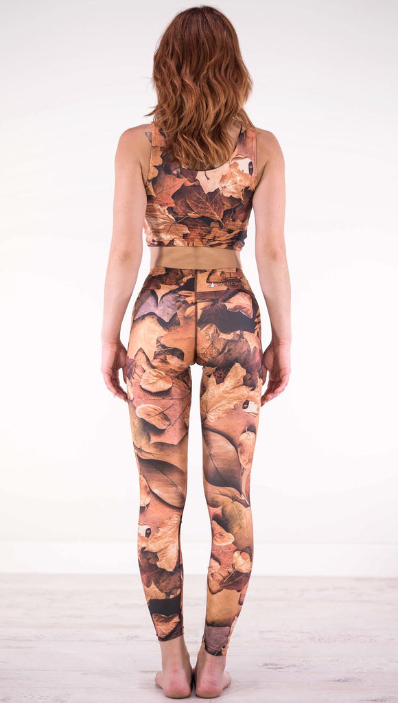 Back view of model wearing traithlon leggings that have different shades of orange autumn leaves
