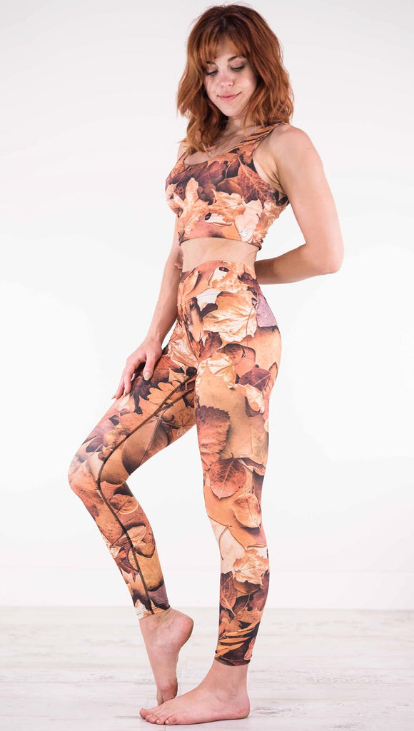 Left view of model wearing triathlon leggings that have different shades of orange autumn leaves