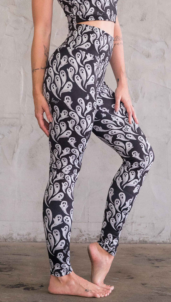 Right view of model wearing black athleisure leggings with little white ghosts and the word "Boo!" in a repeat pattern 