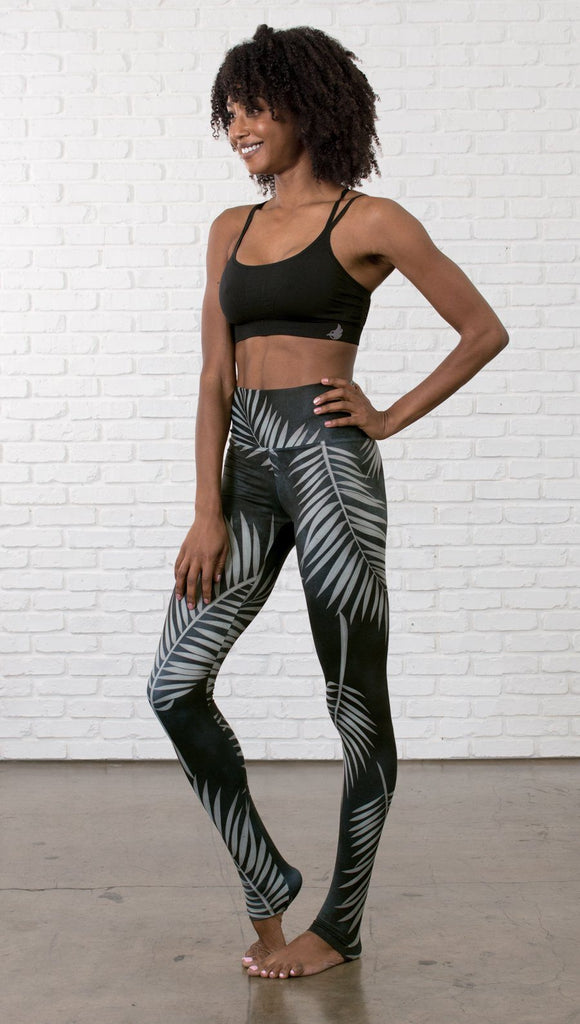 slightly turned front view of model wearing full length black leggings with white palm design and  sports top