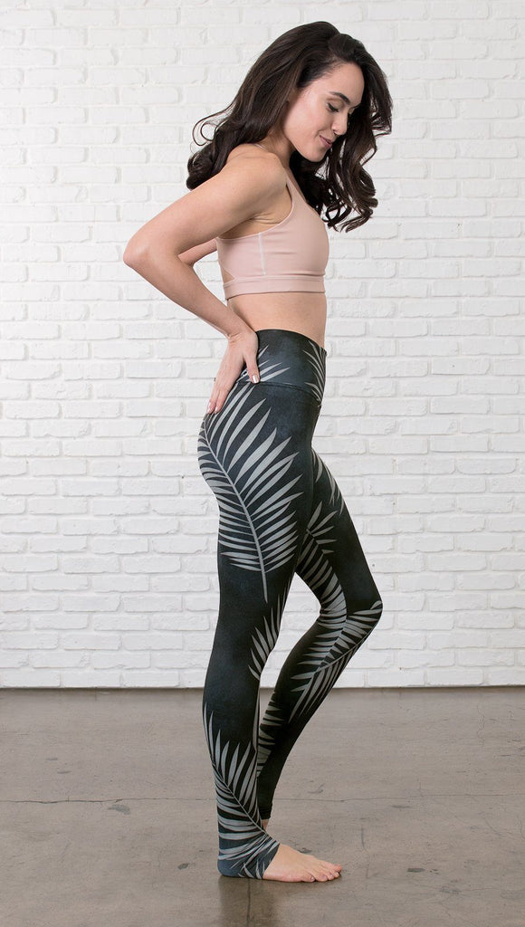 right side view of model wearing full length black leggings with white palm design and sports top