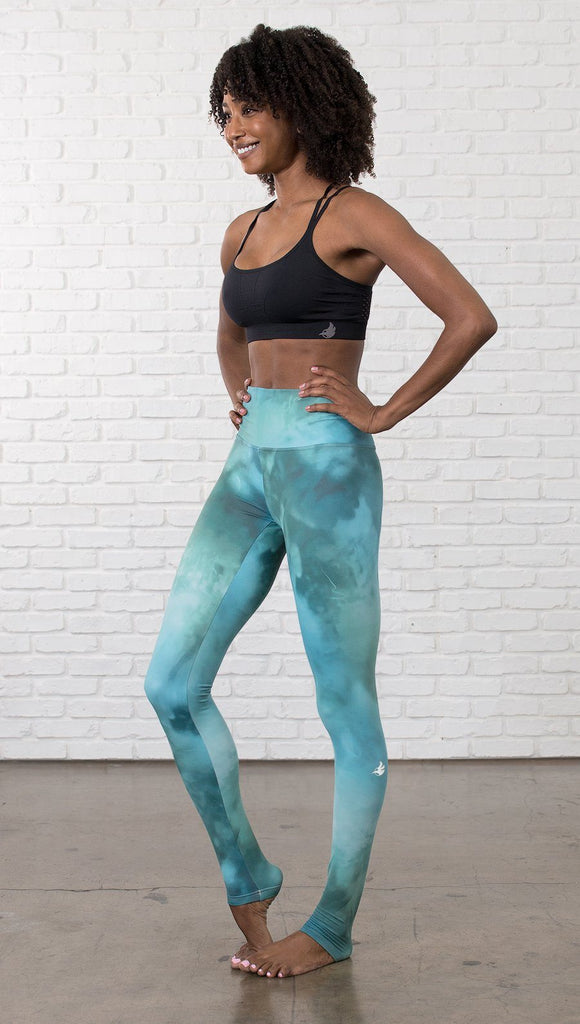 slightly turned view of model wearing water / ocean themed printed full length leggings with black sports top