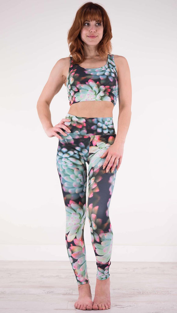 Front view of model wearing black athleisure leggings with green succulent plants with pink tips throughout and the matching top