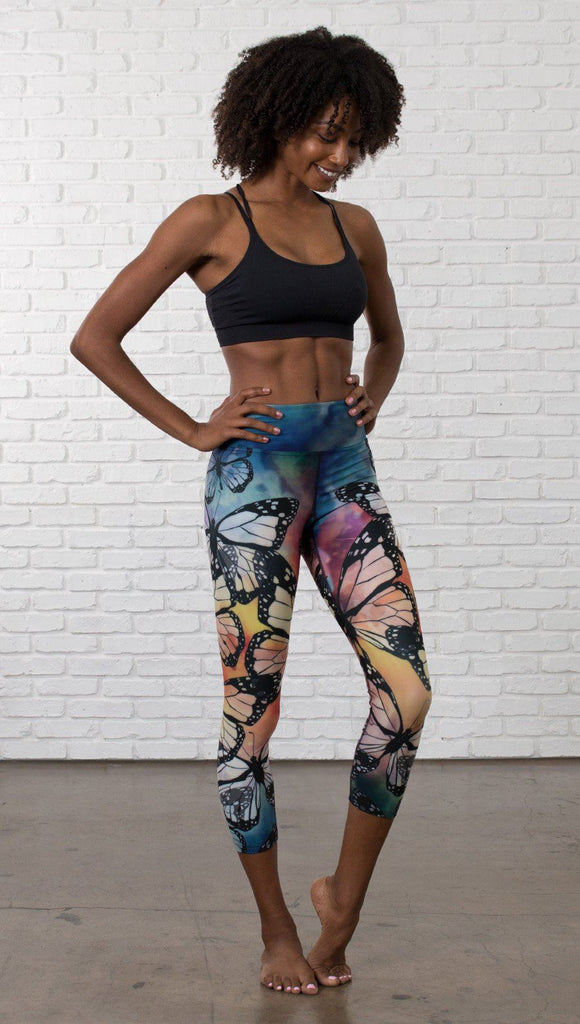 slightly turned front view of model wearing colorful butterfly themed printed capri triathlon leggings