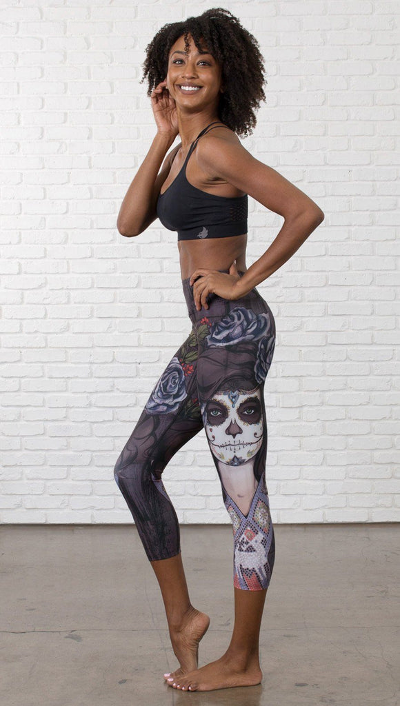 left side view of model wearing sugar skull themed printed capri leggings
