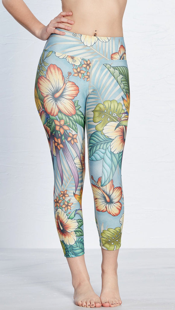 front view of model wearing printed capri leggings with tropical floral design and blue background