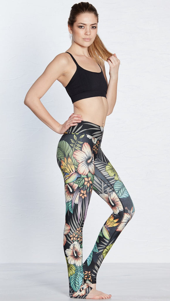 right side view of model wearing printed full length leggings with tropical floral design and black background
