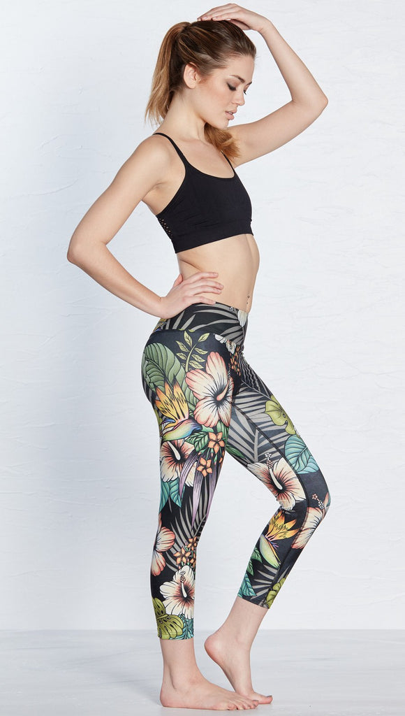 right side view of model wearing printed capri leggings with tropical floral design and black background