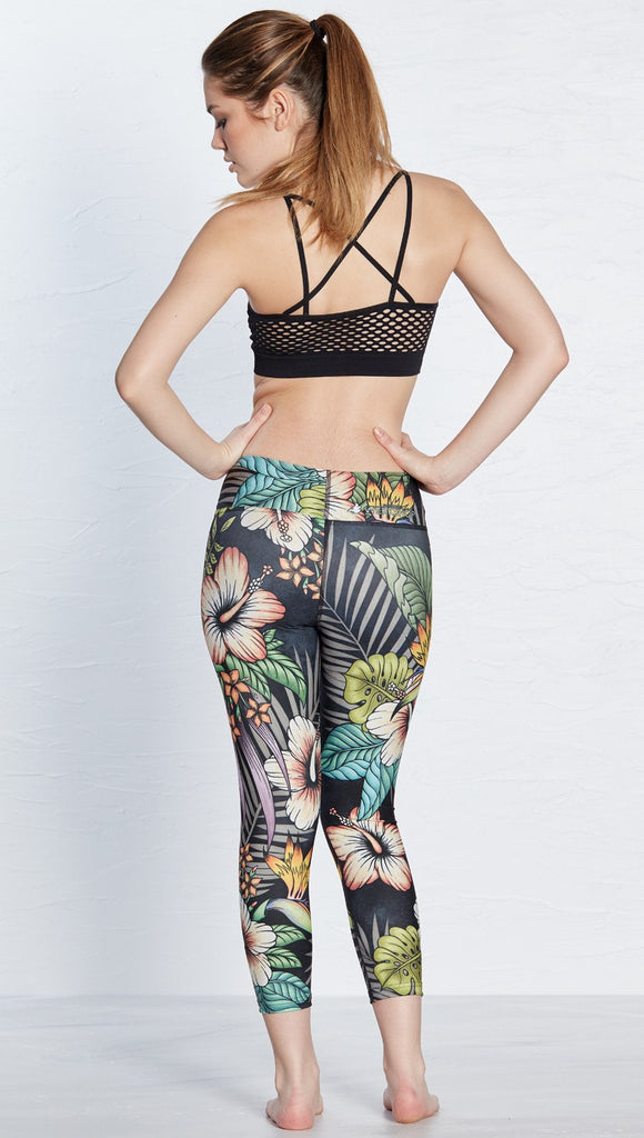 back view of model wearing printed capri leggings with tropical floral design and black background