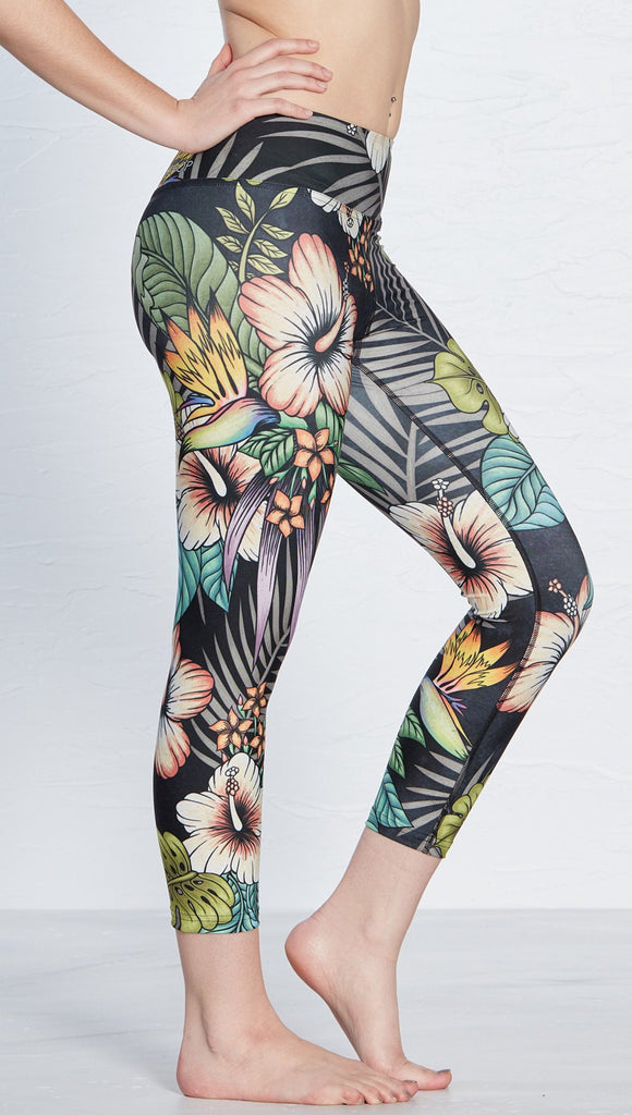 close up right side view of model wearing printed capri leggings with tropical floral design and black background