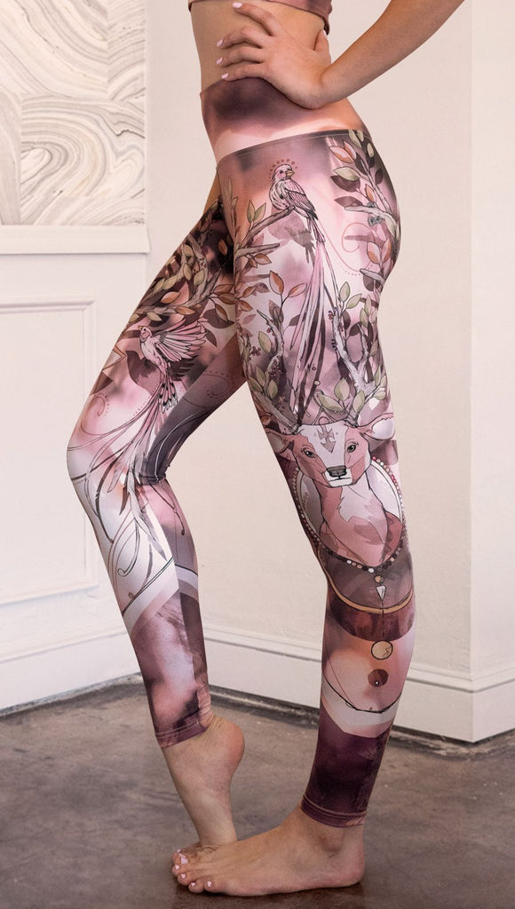 Left side view of model wearing full length athleisure leggings with a deer on it. They are a purple and orange color with tree branches as the antlers and birds on the antlers