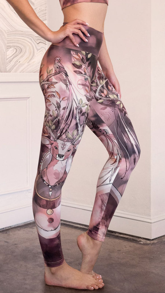 Right  side view of model wearing full length athleisure leggings with a deer on it. They are a purple and orange color with tree branches as the antlers and birds on the antlers