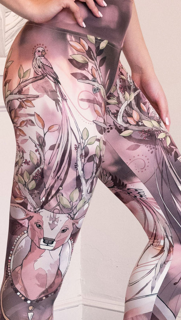Zoomed in right view of model wearing full length athleisure leggings with a deer on it. They are a purple and orange color with tree branches as the antlers and birds on the antlers