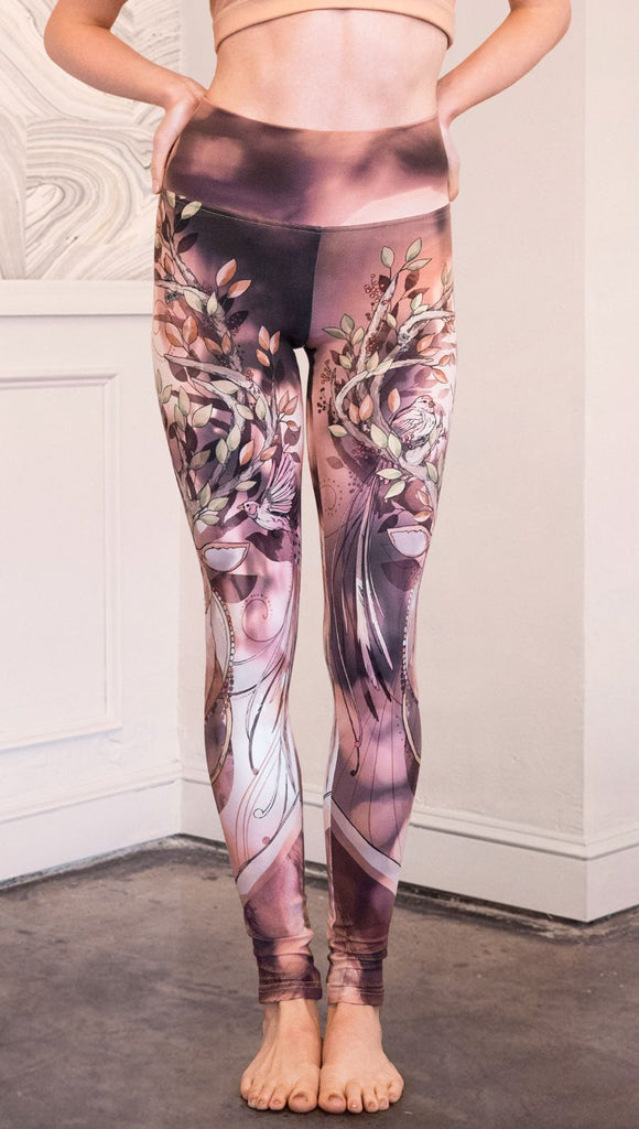 Front view of  model wearing full length athleisure leggings with a deer on it. They are a purple and orange color with tree branches as the antlers and birds on the antlers