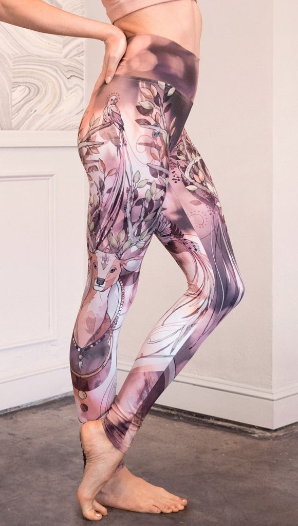 Right view of model wearing full length athleisure leggings with a deer on it. They are a purple and orange color with tree branches as the antlers and birds on the antlers