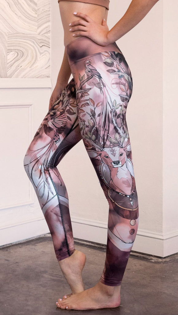 Left side view of model wearing full length triathlon leggings with a deer on it. They are a purple and orange color with tree branches as the antlers and birds on the antlers