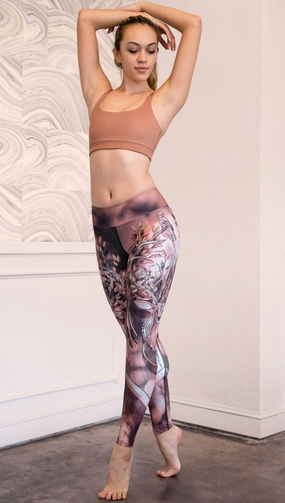 Slightly turned front view of model wearing full length triathlon leggings with a deer on it. They are a purple and orange color with tree branches as the antlers and birds on the antlers