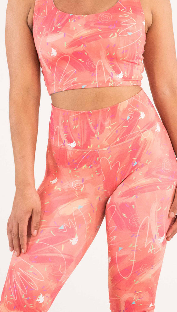 zoomed in front view of model wearing WERKSHOP Salmon Scribble Leggings with coral brushstrokes over a bright salmon background. Also has little confetti and eagle logos scattered throughout.