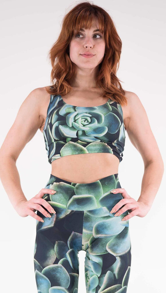 Front view of model wearing the reversible Coachella Sunset Top. This is the Green Envy side, it is a black crop top with green succulent plants throughout