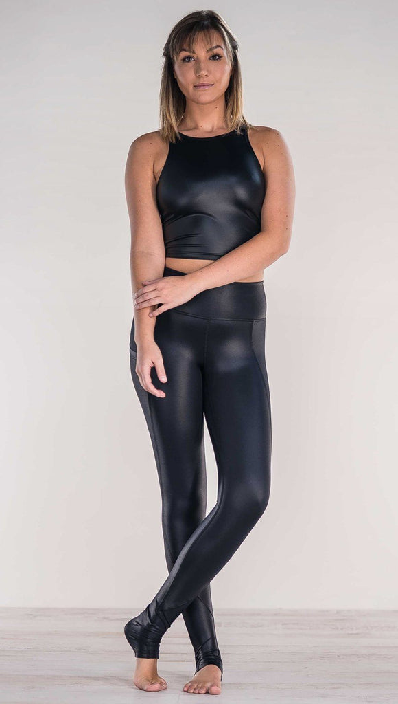 Front view of model crossing ankles wearing shiny black full length leggings with right side pocket