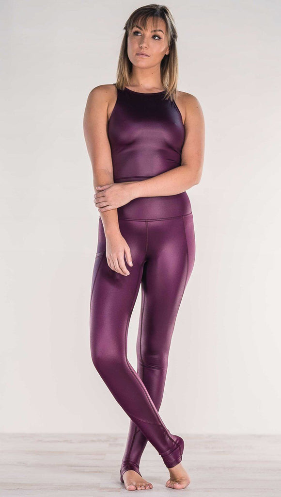 Front view of model crossing ankles wearing shiny eggplant purple colored full length leggings with right side pocket