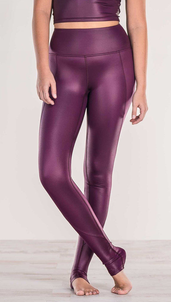 Close up front view of model crossing ankles wearing shiny eggplant purple colored full length leggings with right side pocket