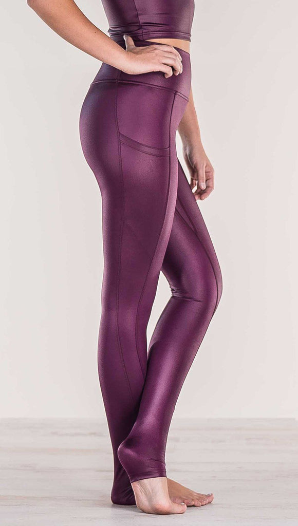 Close up side view of model wearing shiny eggplant purple colored full length leggings with right side pocket