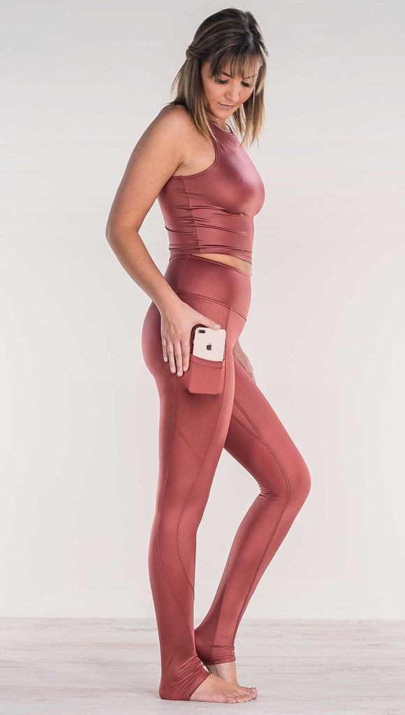 Side view of model wearing shiny mauve full length leggings putting iphone into right side pocket