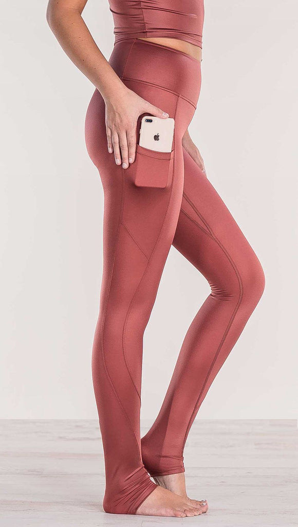 Close up side view of model wearing shiny mauve full length leggings putting iphone into right side pocket