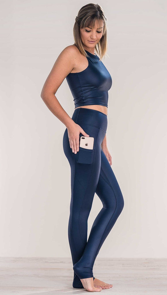 Side view of model wearing shiny midnight blue full length leggings putting iphone into right side pocket