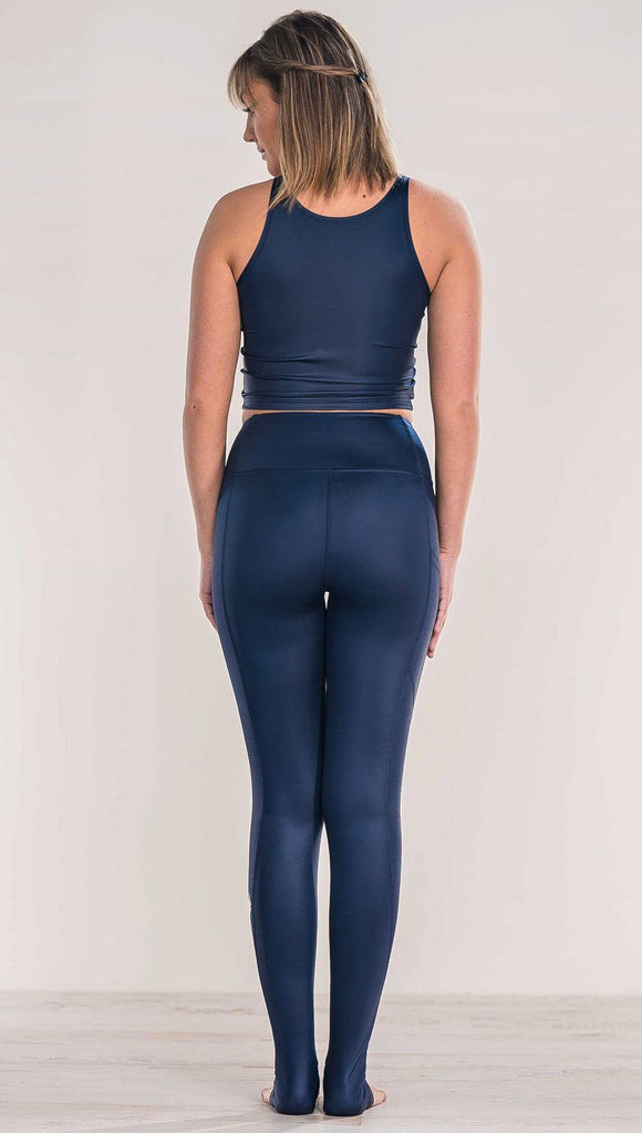 Rear view of model wearing shiny midnight blue full length leggings with right side pocket